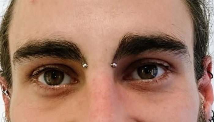 Homme portant un piercing bridge avec deux embouts métalliques chez Atyka Body Works à Toulouse