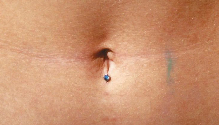 Micro-piercing discret avec bijou bleu posé au niveau du nombril chez Atyka Body Works à Toulouse